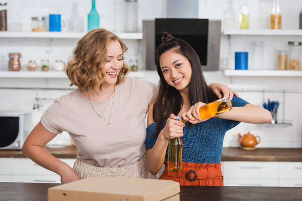 joyful asian woman opening bottles of beer near friends during party