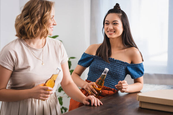 young multicultural women talking while holding beer during party