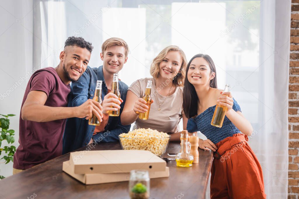 joyful multiethnic friends looking at camera while holding bottles of beer 