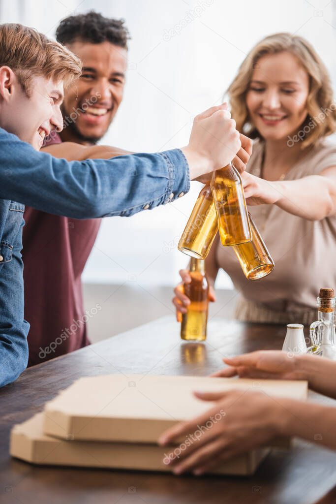 selective focus of multicultural friends clinking bottles of beer during party
