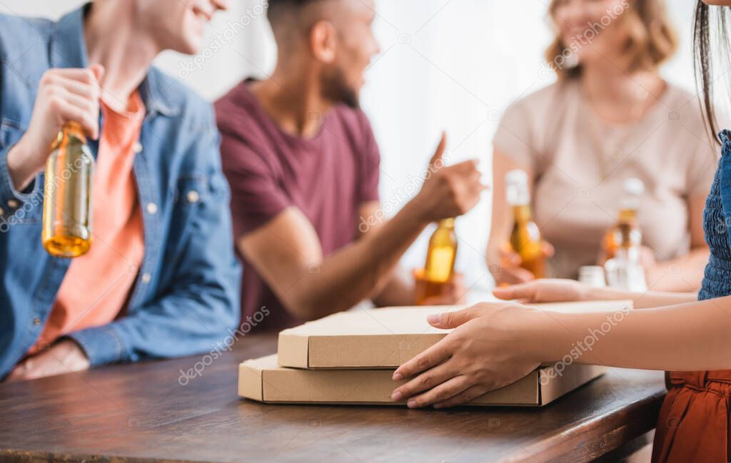 cropped view of woman near pizza boxes and multicultural friends with beer on background