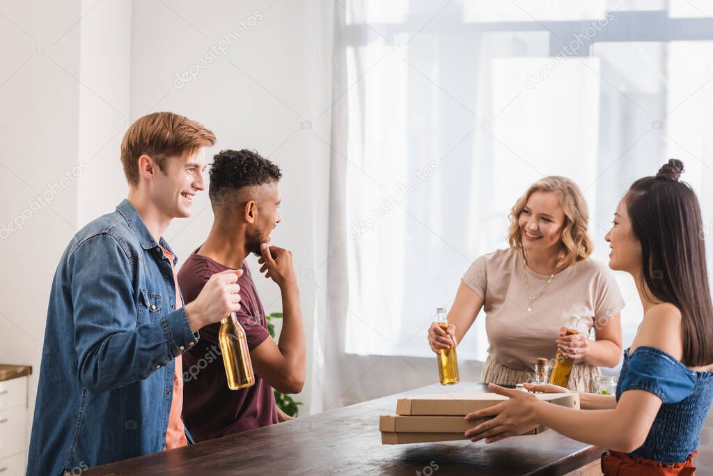 joyful multicultural friends holding beer and pizza boxes during party