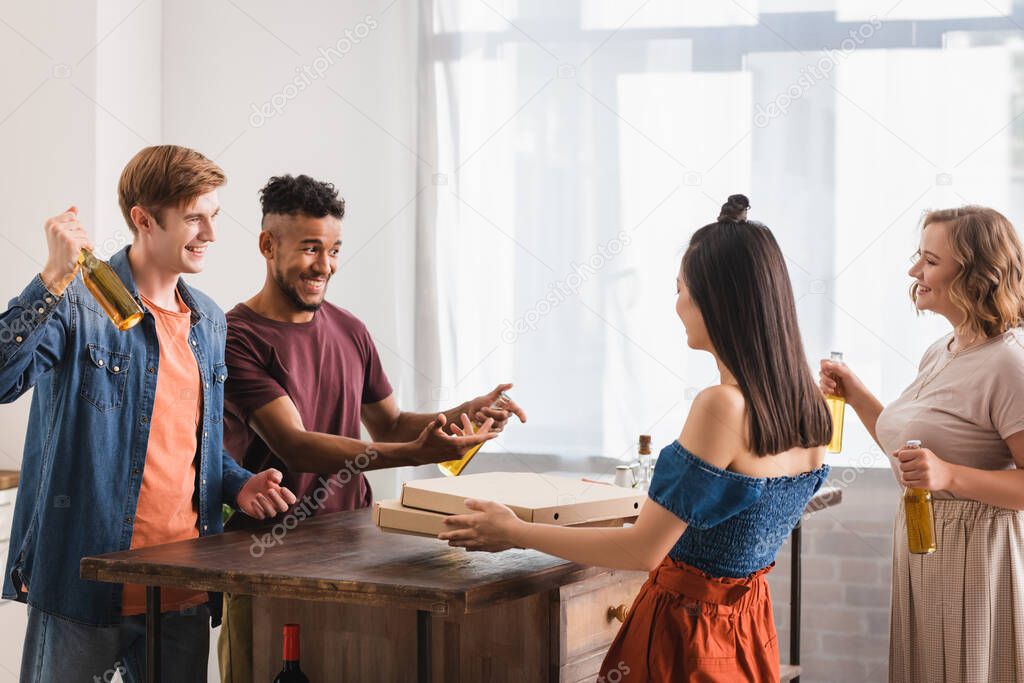 excited multicultural friends holding beer and pizza boxes during party