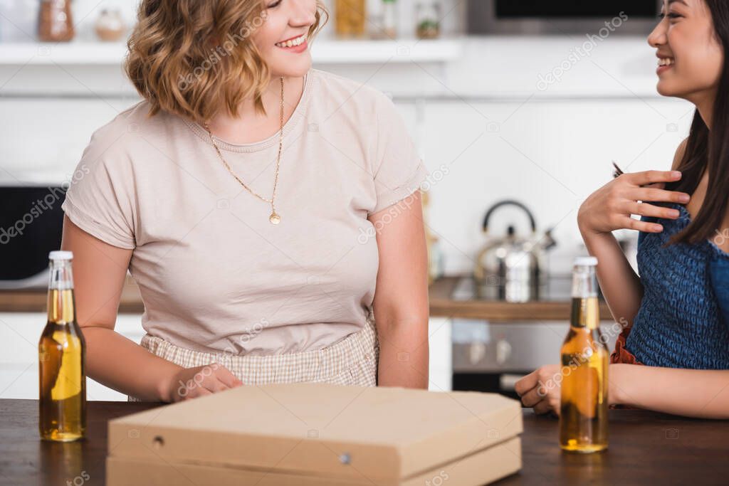 cropped view of multiethnic friends talking near beer and pizza box during party