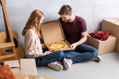 Erkek ve kadın paketler ve akustik gitarın yanındaki kutuda pizzaya bakıyorlar.