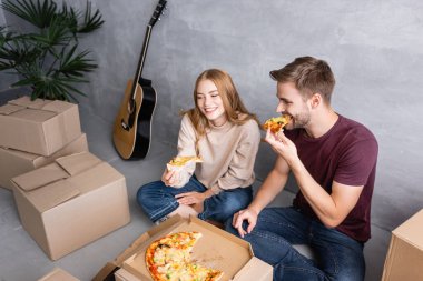 Yüksek açılı bir bakış açısıyla, erkeğin yerde oturup kadın ve kutuların yanında pizza yemesi, taşınma konsepti.