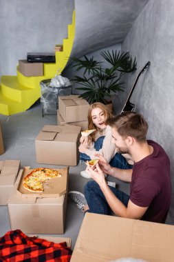 Ağzını açıp elinde pizza olan erkek arkadaşına bakan bir kadın.