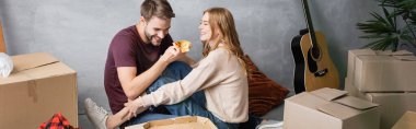 Kadın ve karton kutuların yanında pizza tutan memnun bir adamın panoramik mahsulü