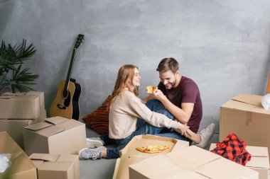 Kadının yanında pizza tutan memnun bir adam ve evde kutular, taşınma konsepti.