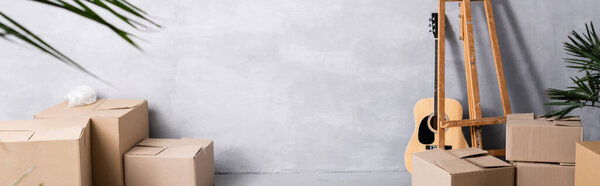 horizontal image of carton boxes near easel, acoustic guitar and plants 