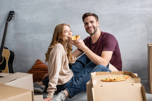 Homem Alegre Alimentando Namorada Satisfeito Com Pizza Perto Caixas Papelão — Fotografia de Stock