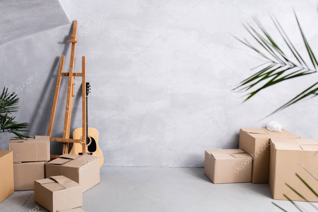 carton boxes near easel, acoustic guitar and plants 