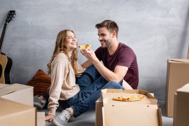 Kız arkadaş ve karton kutuların yanında lezzetli pizzalar tutan neşeli adamın seçici odak noktası, taşınma konsepti