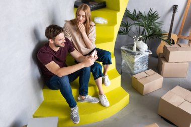 Adam merdivenlerde kız arkadaşı ve karton kutularıyla otururken akıllı telefon kullanıyor.