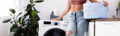 Webové stránky záhlaví mladé ženy držící koš na prádlo v blízkosti pračky v kuchyni 