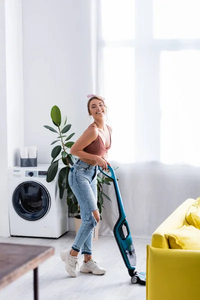 Moderne Huisvrouw Met Stofzuiger Zoek Naar Camera Buurt Van Plant — Stockfoto