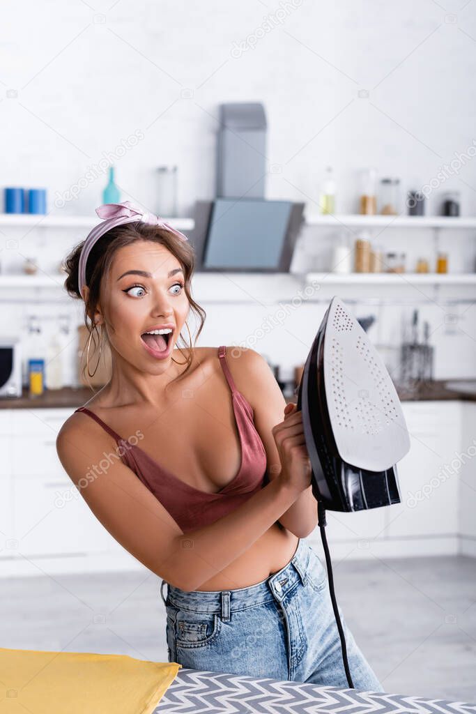 Excited woman holding iron near cloth on ironing board 