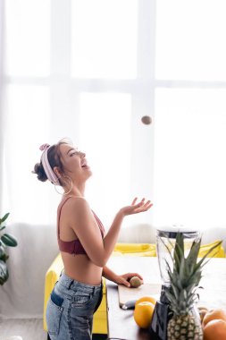 Genç ev kadınının kesim tahtası ve blenderin yanına kivi attığı seçici odak noktası 