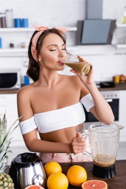 Kadınların meyve suyu içerken mutfak masasındaki meyvelerin yanında blender tuttuğu seçici odak noktası. 