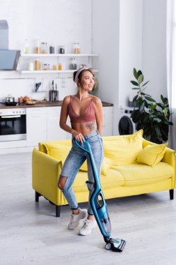 Genç kadın evini elektrikli süpürgeyle temizlerken gözlerini kaçırıyor. 