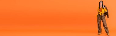 Sonbahar kıyafetli bir kadının turuncu üzerine deri ceket giydiği panoramik oryantasyon. 