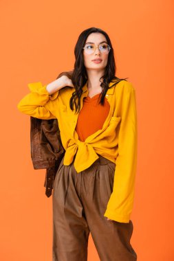 Gözlüklü, sonbahar kıyafetli, deri ceketli, turuncu elbiseli moda bir kadın. 