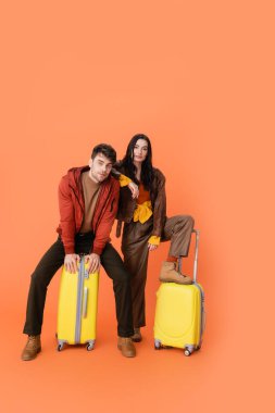 Sonbahar kıyafetli, turuncu üzerinde sarı valizli şık bir çift. 