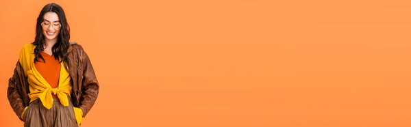 панорамный урожай молодой женщины в осеннем наряде, стоящей с руками в карманах на оранжевом 