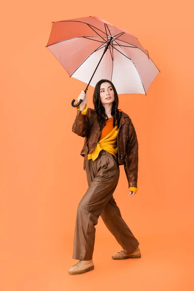 全身上下都是穿着秋装 脚踩着雨伞走在橙色路上的时髦女人 — 图库照片