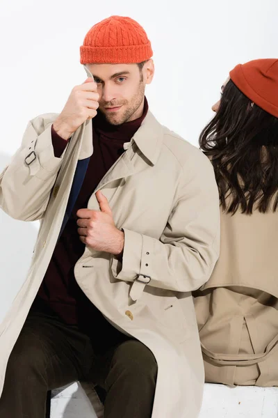 Hombre Elegante Tocando Gabardina Cerca Mujer Gorro Sombrero Sentado Aislado — Foto de Stock