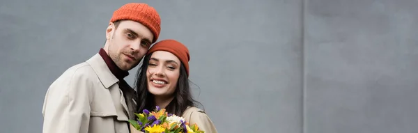 Raccolto Panoramico Coppia Alla Moda Trench Cappelli Vicino Bouquet Fiori — Foto Stock