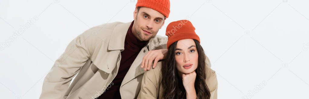 panoramic concept of trendy man in beanie hat leaning on brunette woman isolated on white 