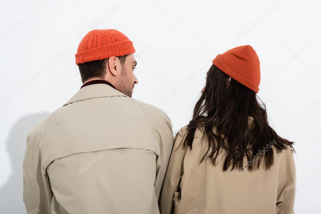 back view of couple in beanie hats and trench coats on white 