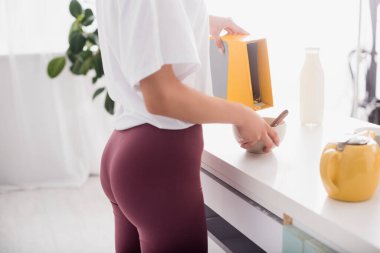 Şortlu genç bir kadının mısır gevreğini kaseye dökerkenki görüntüsü