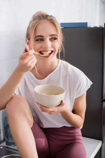 Mulher Loira Alegre Comer Flocos Milho Enquanto Sentado Mesa Cozinha — Fotografia de Stock