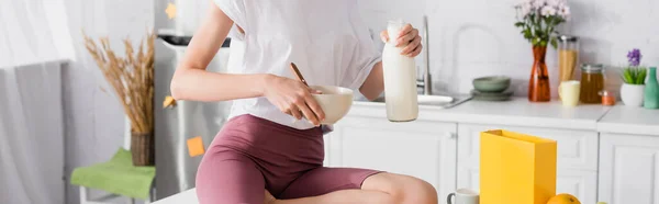 台所で牛乳とボウルを持っている若い女性のクロップドビュー パノラマの概念 — ストック写真