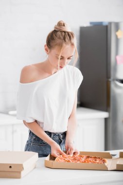 Seçici odak noktası genç sarışın kadın mutfaktaki kutudan pizza alıyor.