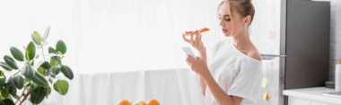 Mutfakta pizza tutarken akıllı telefondan sohbet eden genç bir kadının web sitesi başlığı