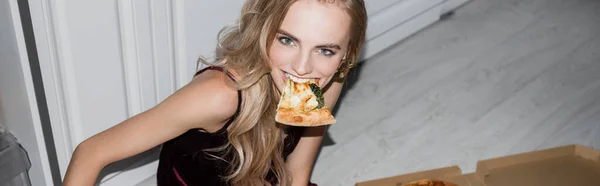 カメラを見ながらピザを食べる陽気なブロンドの女性のパノラマの概念 — ストック写真