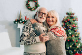 šťastný starší pár objímání při pohledu na kameru s vánoční výzdobou na pozadí