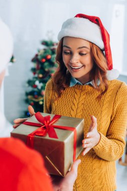 Noel Baba şapkalı heyecanlı kadının seçici odağı kocasından Noel hediyesi alıyor.