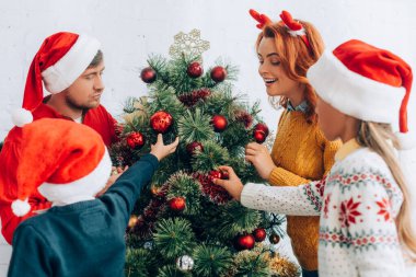 Noel Baba şapkalı mutlu aile evde birlikte Noel ağacı süslüyorlar.