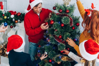 Noel Baba şapkalı mutlu aile evde birlikte Noel ağacı süslüyorlar.