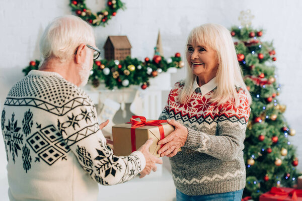 пожилая женщина представляет подарочную коробку с рождественским украшением на заднем плане
