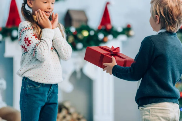 Boy Presenting Christmas Gift Amazed Sister Holding Hands Face — Stock Photo, Image