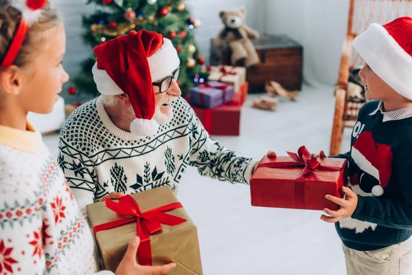 サンタ ハットの高齢者の選択的焦点は孫からクリスマスプレゼントを取り — ストック写真