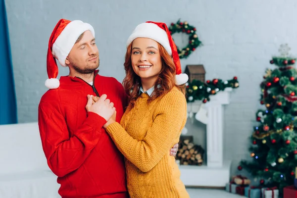 Happy Woman Santa Hat Looking Camera While Embracing Husband Christmas — Stock Photo, Image