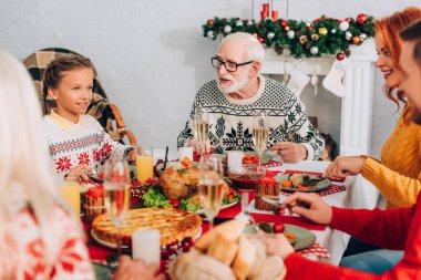 Selective focus of happy family sitting at festive table near decorated fireside clipart