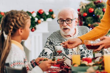 Selective focus of grandfather talking to girl at festive table near fireplace clipart