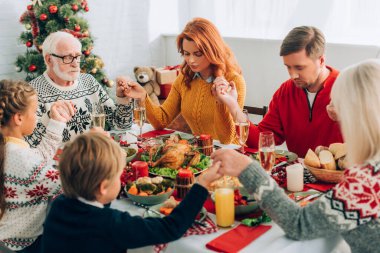 Family holding hands while sitting at festive table with thanksgiving dinner clipart